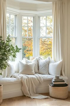 a white window seat with pillows and blankets on it in front of a potted plant