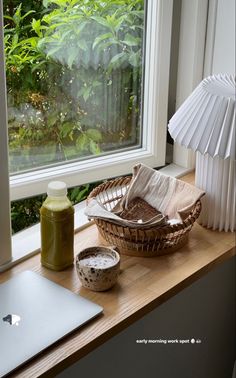 a laptop computer sitting on top of a wooden desk next to a basket and cup