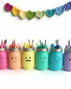 colorful mason jars with crocheted faces and pencils in them are lined up against a white wall