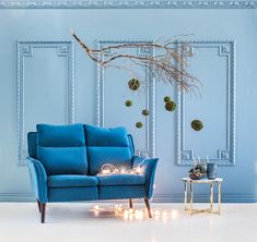 a blue couch sitting next to a table with candles on it in front of a wall