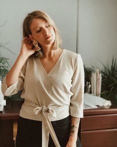 a woman standing in front of a desk talking on a cell phone and holding her hand up to her ear