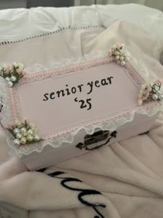 a pink and white box sitting on top of a bed with a sign that says senior year