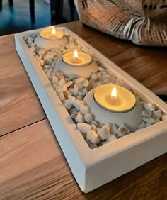 three lit candles sit in a decorative water feature on a wooden table next to a wicker basket