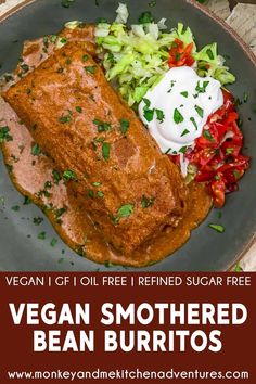 vegan smothered bean burritos on a plate with vegetables and sour cream