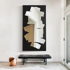 a black and white painting hangs on the wall next to a bench in front of a mirror