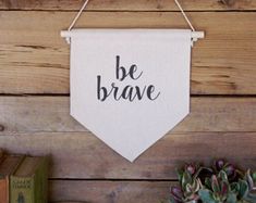 a white banner hanging on a wooden wall that says be brave