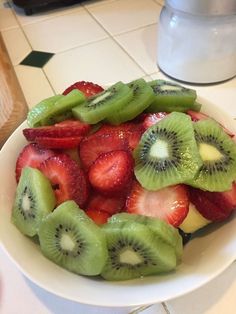 a white bowl filled with sliced kiwi and strawberries on top of a counter