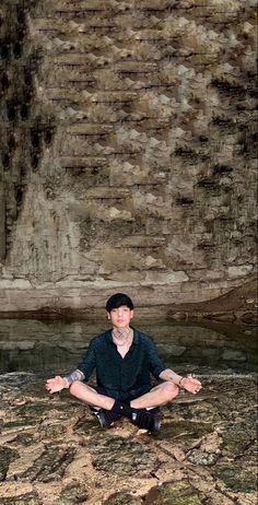 a man sitting on the ground in front of a stone wall with his hands crossed