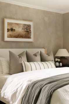 a bed with white sheets and pillows in a bedroom next to a painting on the wall