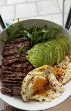 a white plate topped with steak, eggs and an avocado