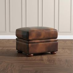 a brown leather ottoman sitting on top of a hard wood floor next to a white wall