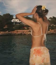 a woman standing in the water with her back to the camera and wearing a flower in her hair