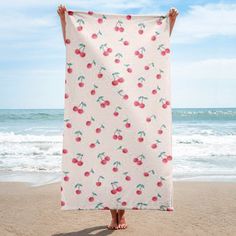 a person standing on the beach holding up a towel with cherries all over it