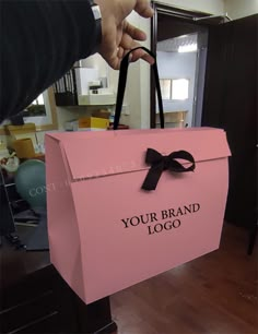 a person is holding a pink bag with a black bow on it that says your brand logo