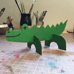 a green wooden toy alligator sitting on top of a table next to paintbrushes