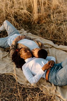 two people laying on a blanket in the middle of a field with tall dry grass