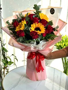 a bouquet of sunflowers and roses wrapped in pink paper on top of a table