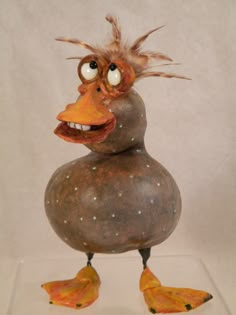 a sculpture of a duck with feathers on its head and legs, standing in front of a white background