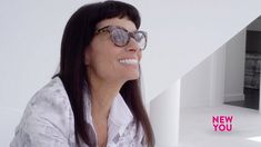 a woman wearing glasses sitting in front of a white wall with the words new you on it