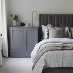 a bedroom with a gray headboard, white bedding and grey cabinet in the corner