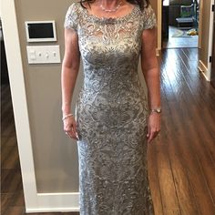 a woman standing in a room wearing a long silver dress with an intricate pattern on it