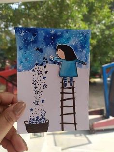 someone holding up a card with a drawing of a girl on a ladder reaching for stars