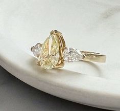 a yellow diamond ring sitting on top of a white marble slab with three diamonds around it