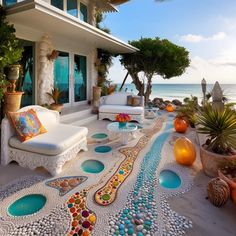 an outdoor living area with white couches and colorful pebbles on the ground next to the ocean