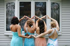 four women standing in front of a window making the shape of a heart with their hands