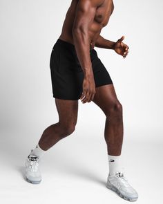 a man with no shirt is posing for the camera wearing black shorts and white sneakers