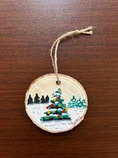 a wooden ornament with a christmas tree painted on it's side hanging from a string