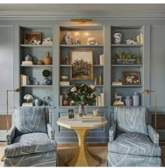 two chairs and a table in a room with built - in bookshelves on the wall