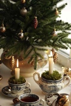 a table topped with cups and saucers covered in christmas decorations next to a small tree