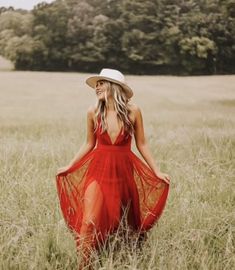 a woman in a red dress and hat walking through tall grass