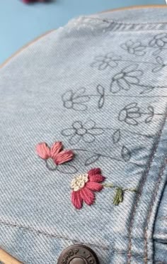 the back side of a jean jacket with embroidered flowers on it and a button at the bottom