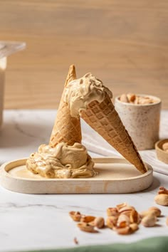 two ice cream cones with peanut butter on top and some nuts in the bottom, sitting on a marble tray