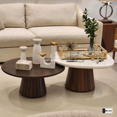 two coffee tables with vases on them in front of a white couch and chair