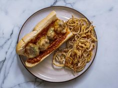 a white plate topped with a hot dog covered in toppings next to some noodles