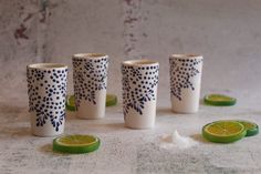 four shot glasses sitting next to each other with limes on the ground in front of them