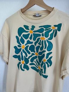 a white t - shirt with blue and yellow flowers painted on it's chest