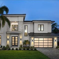 a white two story house with palm trees in the front yard at dusk, lit up by lights