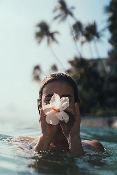 a man floating in the water holding a flower up to his face with both hands