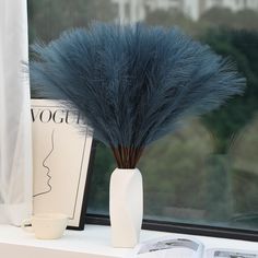 a vase with some blue feathers in it on a window sill next to a book