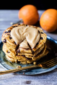 a stack of pancakes with icing on top and two oranges in the background