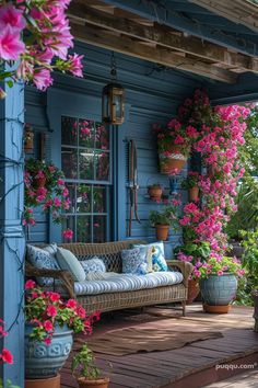 a porch covered in lots of flowers and potted plants next to a blue building