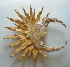 a gold sun and moon face on a white wall with hair blowing in the wind