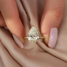 a woman's hand holding a ring with a pear shaped diamond on top of it