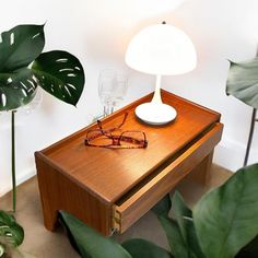 a wooden table with glasses on it next to a green plant and a white lamp