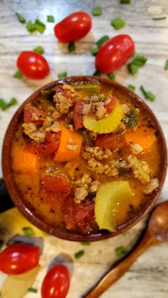 a bowl filled with soup next to spoons and tomatoes