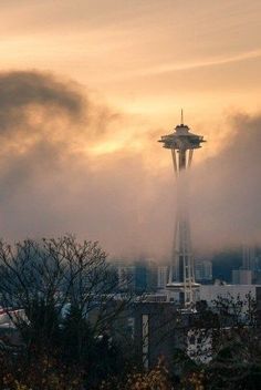 the space needle in seattle is shroud by fog and sunbeams as it peeks through the clouds